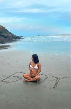 a woman sitting in the sand with her heart drawn in the sand on the beach