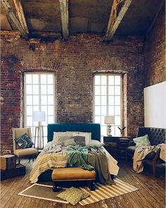 a bedroom with exposed brick walls and wooden flooring is pictured in this image, there are two windows above the bed