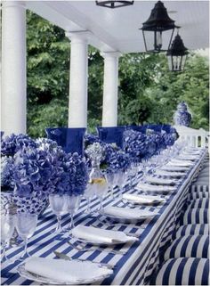 an outdoor dining area with blue and white striped tablecloths, black and white place settings, and hanging lanterns