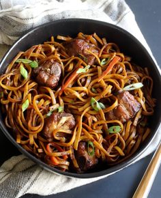 a bowl filled with noodles and meat on top of a table next to chopsticks