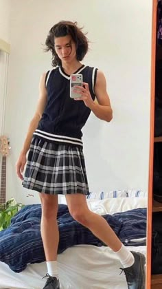 a girl in a skirt is looking at her cell phone while standing on a bed