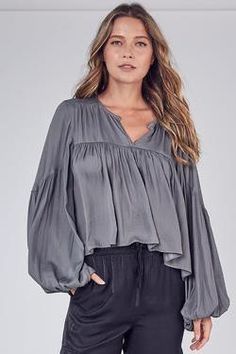 This is the absolute perfect blend of elegance, sexiness and class in one gorgeous, lightweight blouse. It’s loose fitting and flowy but balanced out with a shorter front hem. It’s not a crop, but could show a peak if you really wanted to. With balloon sleeves, a hooked closed neckline and silky feel, you will be the showstopper in any room you enter. Colors: Ash Olive and Orchid Mist Balloon Sleeves Hook Neck Closure Loose Fitting Subtle Mid-back Ruffle 100% Polyester Suggested Care: Hand Wash Flowy Blouse Outfit Classy, Flowy Blouse Outfit, Boho 2024, Boho Long Sleeve Shirt, Swift Outfits, Contemporary Loft, Flowy Shirt, Balloon Sleeve Top, Feminine Top