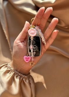 a person holding a cell phone in their hand with charms attached to the back of it