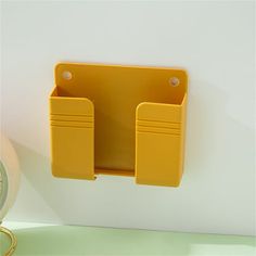 a yellow wall mounted shelf next to a clock on a white wall with two compartments