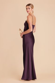 a woman in a long purple dress is standing and looking at the camera with her back turned