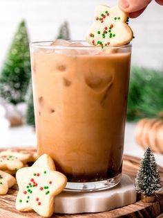 someone is holding a cookie in front of a cup of hot chocolate with cookies on the side