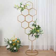 two vases filled with flowers sitting on top of a wooden floor next to a white curtain