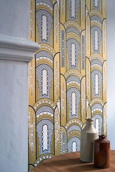 two vases sitting on top of a wooden table next to a wallpapered wall