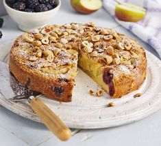 a cake on a plate with one slice cut out and some fruit in the background