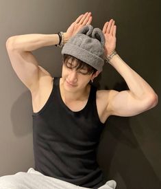 a young man wearing a gray hat and black tank top with his hands on his head