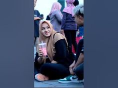 a woman sitting on the ground with a drink in her hand and other people standing around