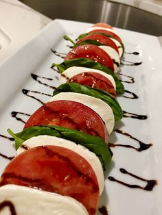 several slices of tomato and mozzarella arranged on a white plate with sauce drizzled over them