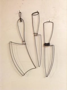 three pieces of wire hang on the wall next to each other, one with a knife and two without