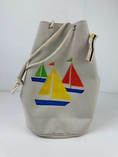 "...be ready to hit the water! THE DETAILS: Off white in color, primary bold sail boat patches, drawstring closure, bucket style bag, lined, material is medium weight with structure ~ Era: 80's ~ Material: canvas ~ Style: Coastal / Preppy / Nautical ~ Condition: Good, no flaws - ready to wear - dirty on top right of bag (probably would wash out very easily/I just don't want to take original tag off to do so) MEASUREMENTS (Flat Lay): ~ Height 12\" ~ Width 12\" ~ Depth 7\" *COMPARE PERSONAL MEASUR Sailor Bags, Coastal Preppy, Boat Beach, Beach Retro, Vintage Bucket, Bucket Bags, Sail Boat, Beach Tote, Perfectly Imperfect