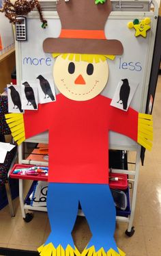 a paper scarecrow is standing in front of a bulletin board