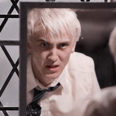 a man with white hair is looking at himself in the mirror and making a face