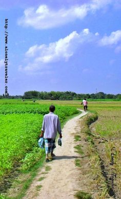 two people walking down a dirt road in the middle of a field