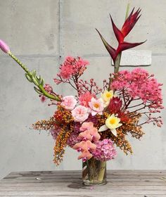 a vase filled with flowers on top of a wooden table next to a cement wall