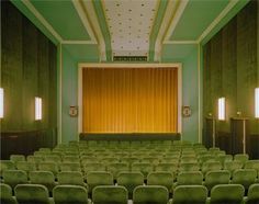 an empty auditorium with rows of green chairs and yellow curtains on the front row,