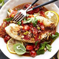 a white plate topped with fish covered in sauce and garnished with lemon wedges