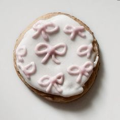 a cookie decorated with pink bows and icing on a white table top, ready to be eaten