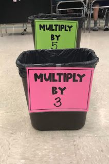 two black trash cans with pink and green labels on them in a room filled with people