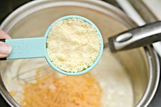 a person holding a measuring spoon over a pot with some food in it and cheese on the side