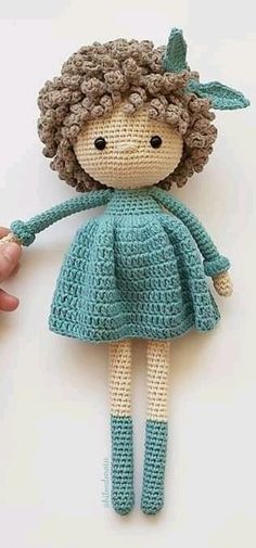 a crocheted doll is being held up by someone's hand on a white surface