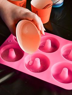 a person pouring orange juice into an ice cream cup in a pink muffin tray