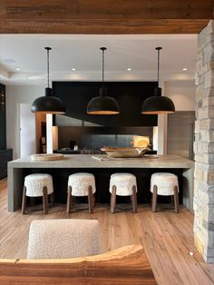 an open kitchen and dining area with stools in front of the counter, lights hanging from the ceiling