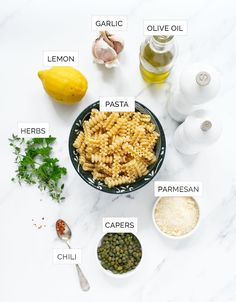 ingredients to make pesto pasta laid out on a white marble counter top, including lemons, parmesan, parmesan and garlic