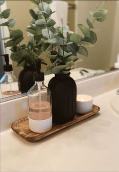 a bathroom counter with two black bottles and a candle on the tray next to it