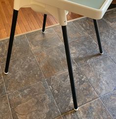 a white plastic chair with black legs on a tile floor next to a wooden table