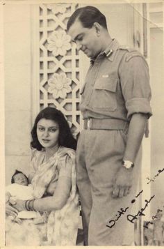 an old black and white photo of a man holding a baby next to a woman