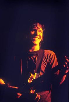 a man holding an electric guitar in his right hand and smiling at the camera,