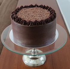 a large chocolate cake sitting on top of a glass platter next to a wooden table