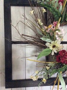 an arrangement of flowers is placed on the wall in front of a mirror with black frame