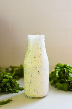 a jar filled with dressing sitting on top of a counter next to some green vegetables