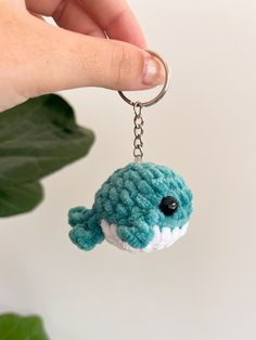 a hand holding a crocheted keychain with a small blue fish on it