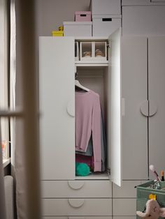 a white cabinet with a pink sweater hanging on it's door and a teddy bear in the corner