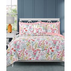 a white bed with pink and green flowers on the comforter in front of a blue wall