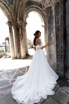 a woman in a white wedding dress standing by an archway