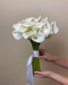 a person holding a bouquet of white flowers with a ribbon tied around the bottom of it