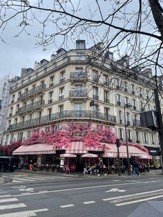 the building has pink flowers on it and people are walking around in front of it