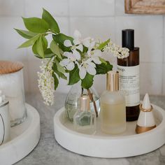 two white vases with flowers in them sitting on a marble counter next to other bottles