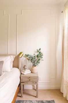 a bed room with a neatly made bed and a plant on the nightstand next to it