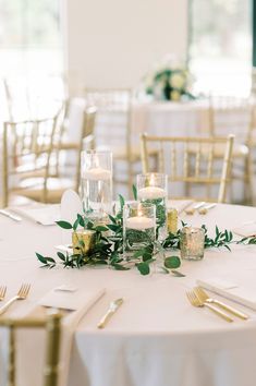 the table is set with candles and greenery for an elegant wedding reception in white linens