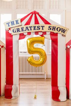 an entrance to the greatest show is decorated in gold and white with a large number 5 balloon