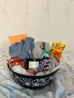 a black bowl filled with lots of different types of food and snacks on top of a bed