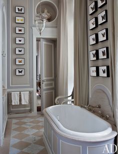 a white bath tub sitting in the middle of a bathroom next to framed pictures on the wall